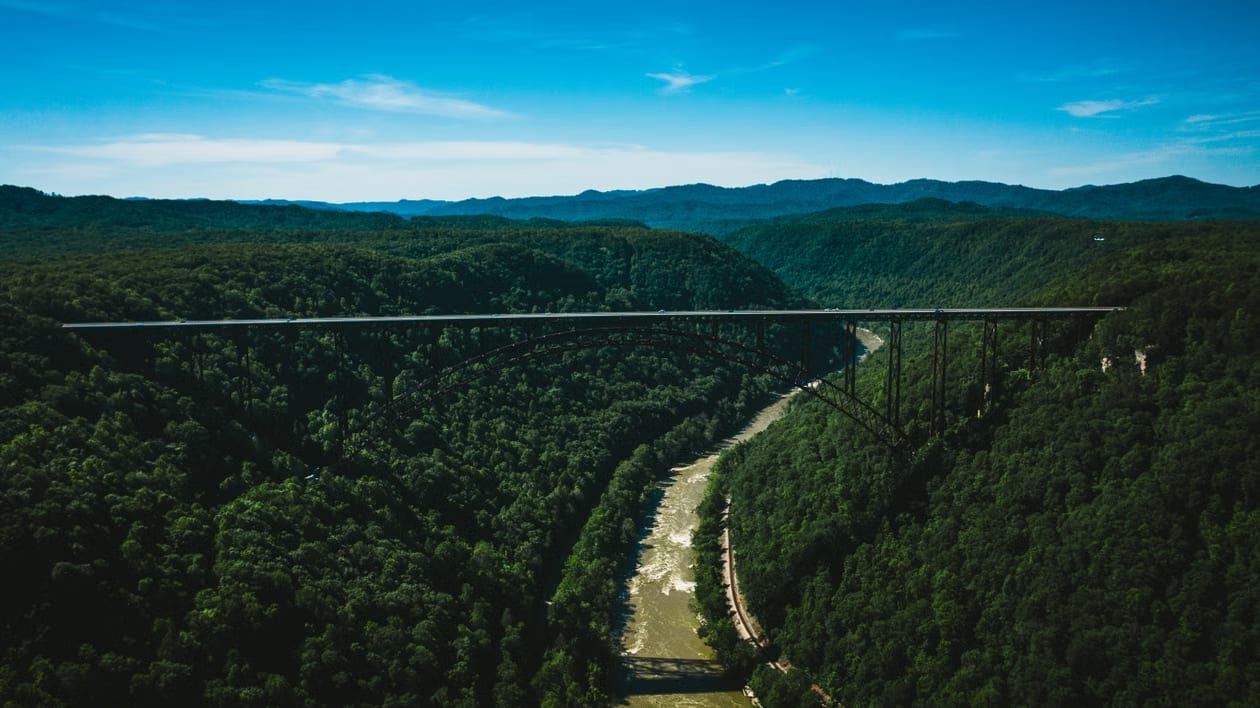 Forested Appalachian gorge in West Virginia with a steel arch bridge spanning the river valley