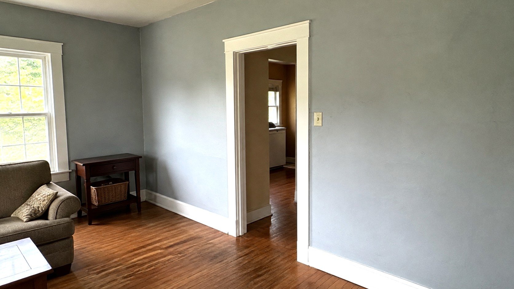 White painted door casing, window trim and baseboard in a blue-grey living room with hardwood floors