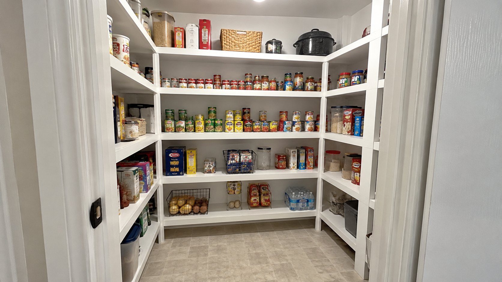 Walk-in pantry with painted wood shelving on three walls, stocked with canned goods